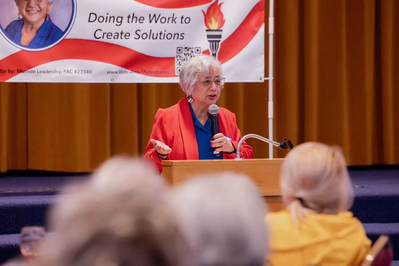 Anna Munson speaking at a podium in front of her campaign banner