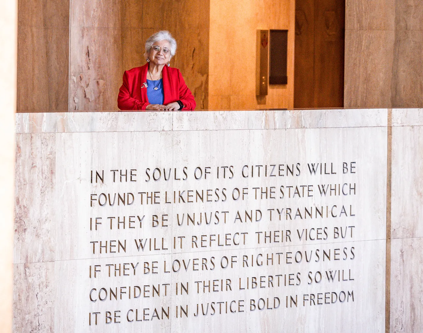 Anna Munson in a red jacket behind a marble wall engraved with the Oregon Capitol’s inscription about citizens and the state