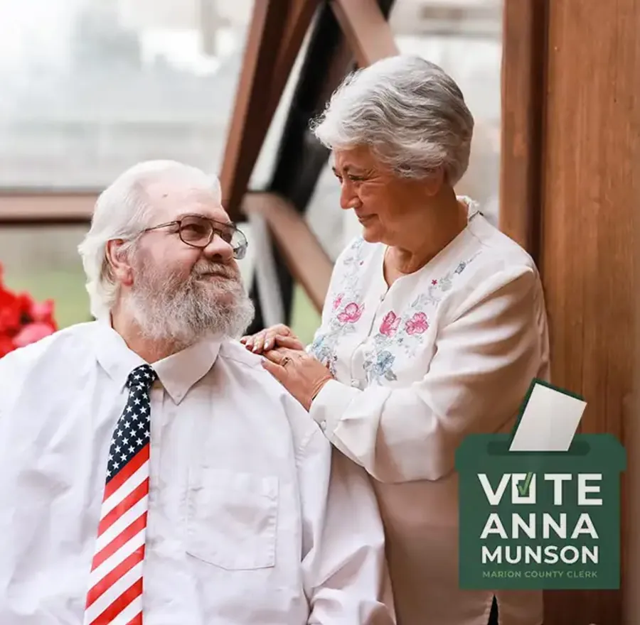 Anna Munson with her husband, who wears a flag-pattern tie, beside a Vote Anna Munson sign